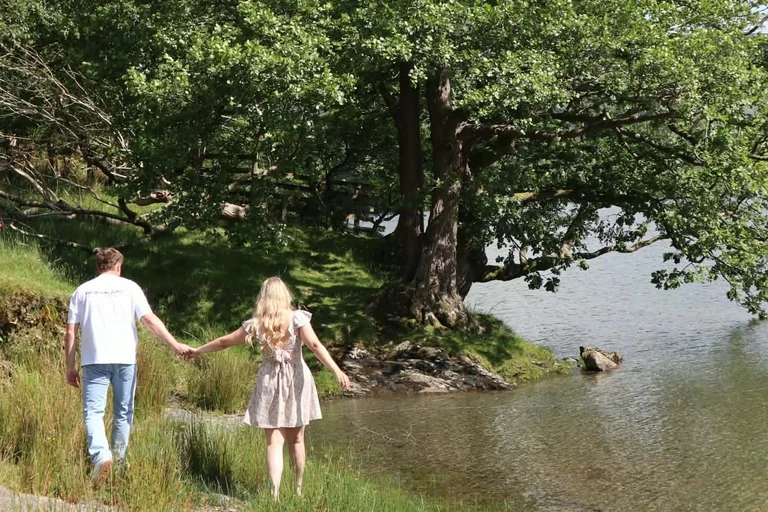 Brad and Naomi walking hand in hand towards a big tree at the water's edge, seen from behind
